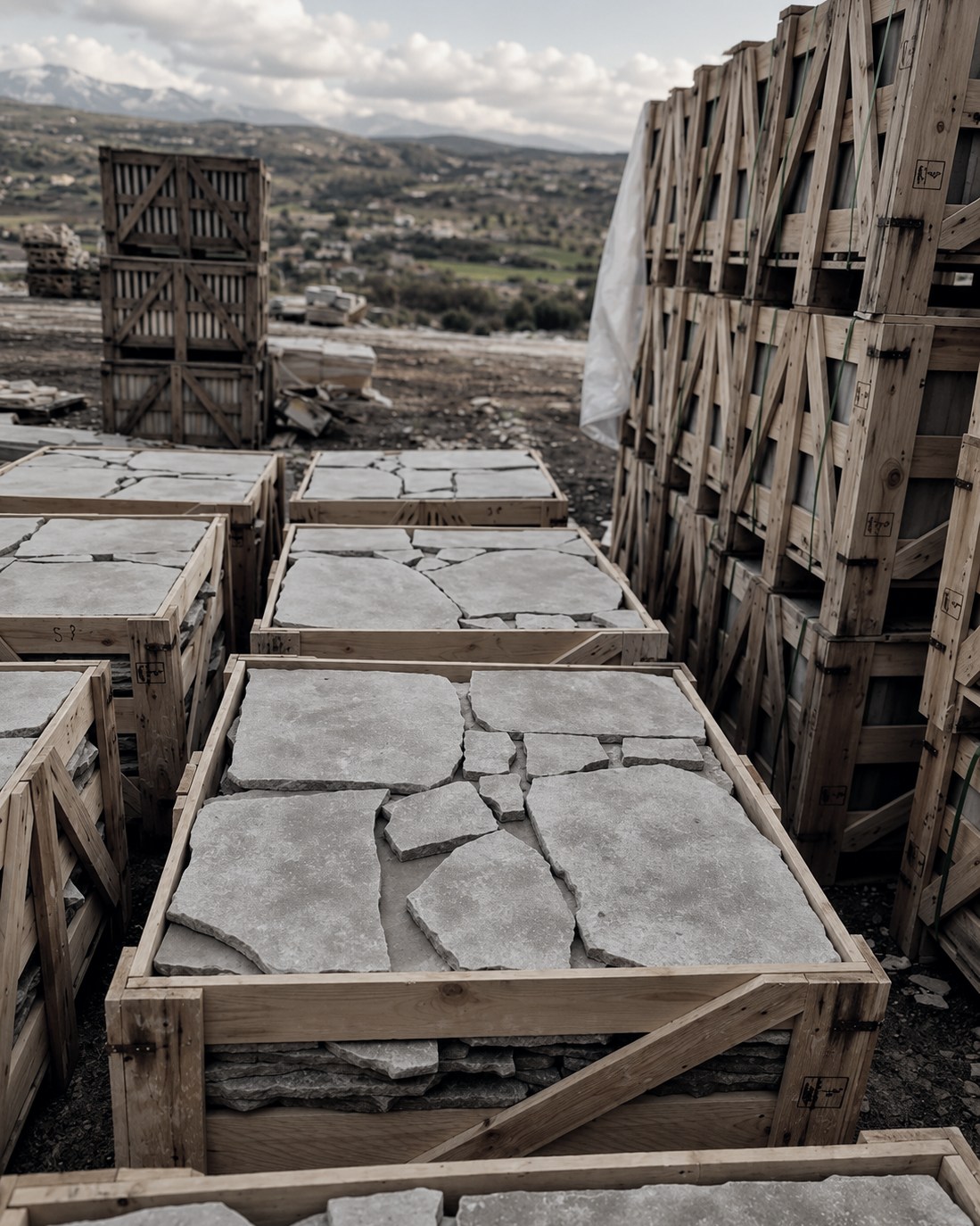 Crates of tumbled crazy paving at the Moroccan quarry yard, valley beyond