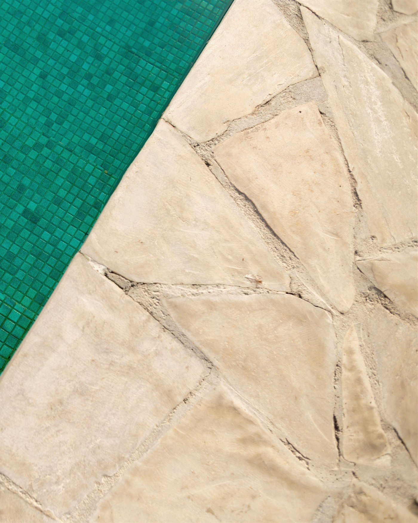 Hand-tumbled crazy paving stone pool surround beside a teal mosaic tiled pool